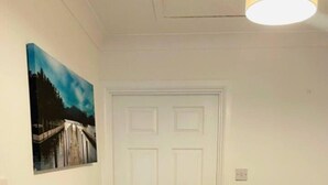 A hallway with a white door, a painting on the wall, and a black carpet. - Lovely 2-bed House in Rochester (Rochester)