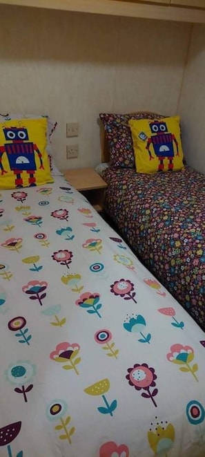 A bed with a floral-patterned bedspread and two pillows, one with a robot design and the other with a floral pattern.