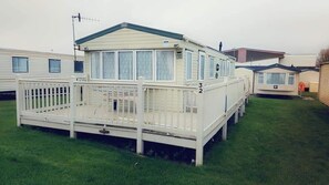 A mobile home with a fenced porch, a small deck, and a number '32' on the side.