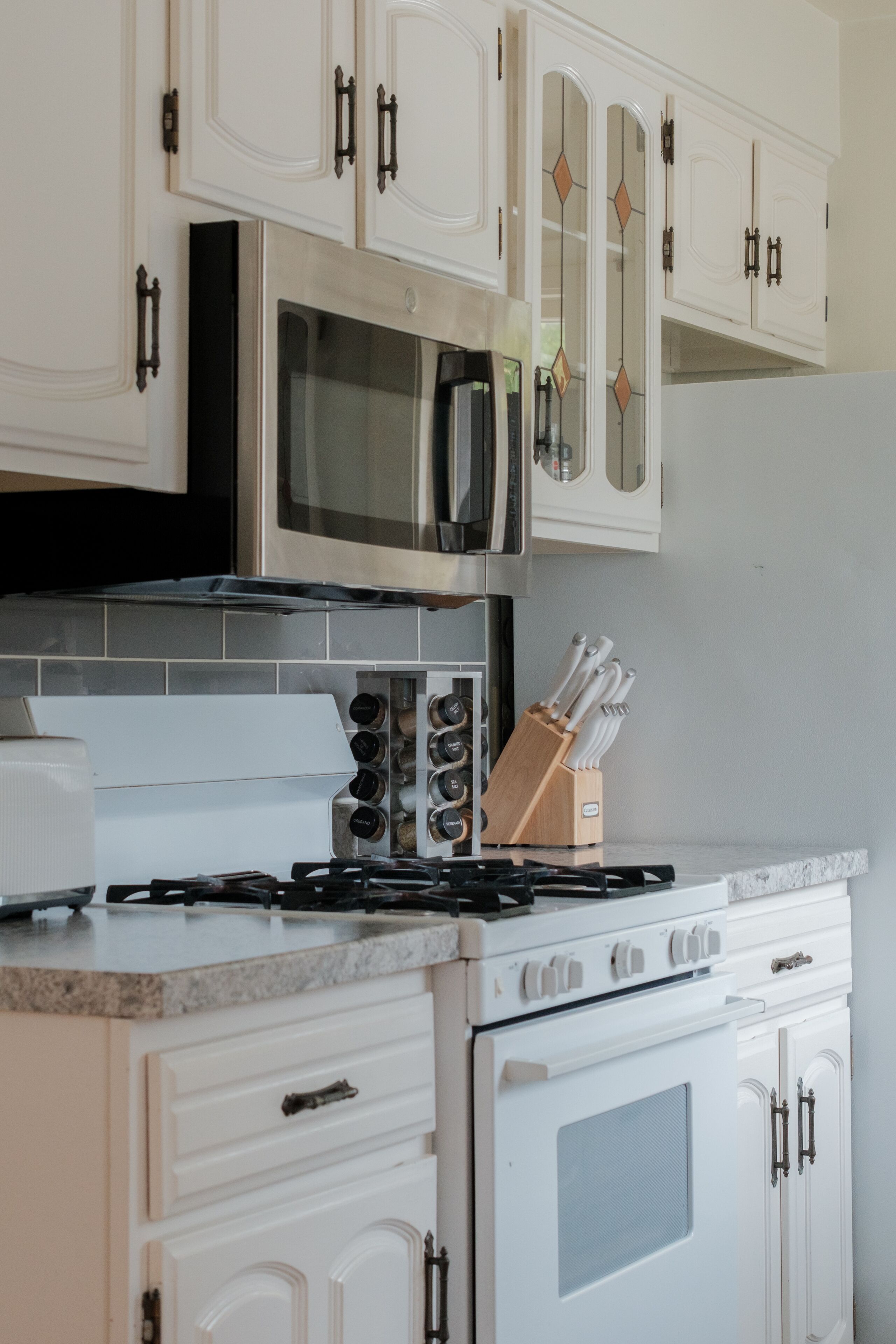 Une cuisine avec des meubles blancs, un four à micro-ondes, une cuisinière et un bloc à couteaux.