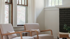 A living room with two beige armchairs, a round wooden coffee table, and a fireplace. - Stylish Family/Pet Friendly Cottage in Coveted Clark Park with Fenced In Yard  (Champaign)