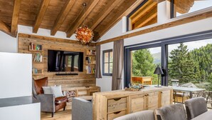 A modern living room with a wooden ceiling, a flat-screen TV, bookshelves, a sofa, and a dining area with a view of the outdoors. - Superior Chalet for 8 people with sauna (Turrach)