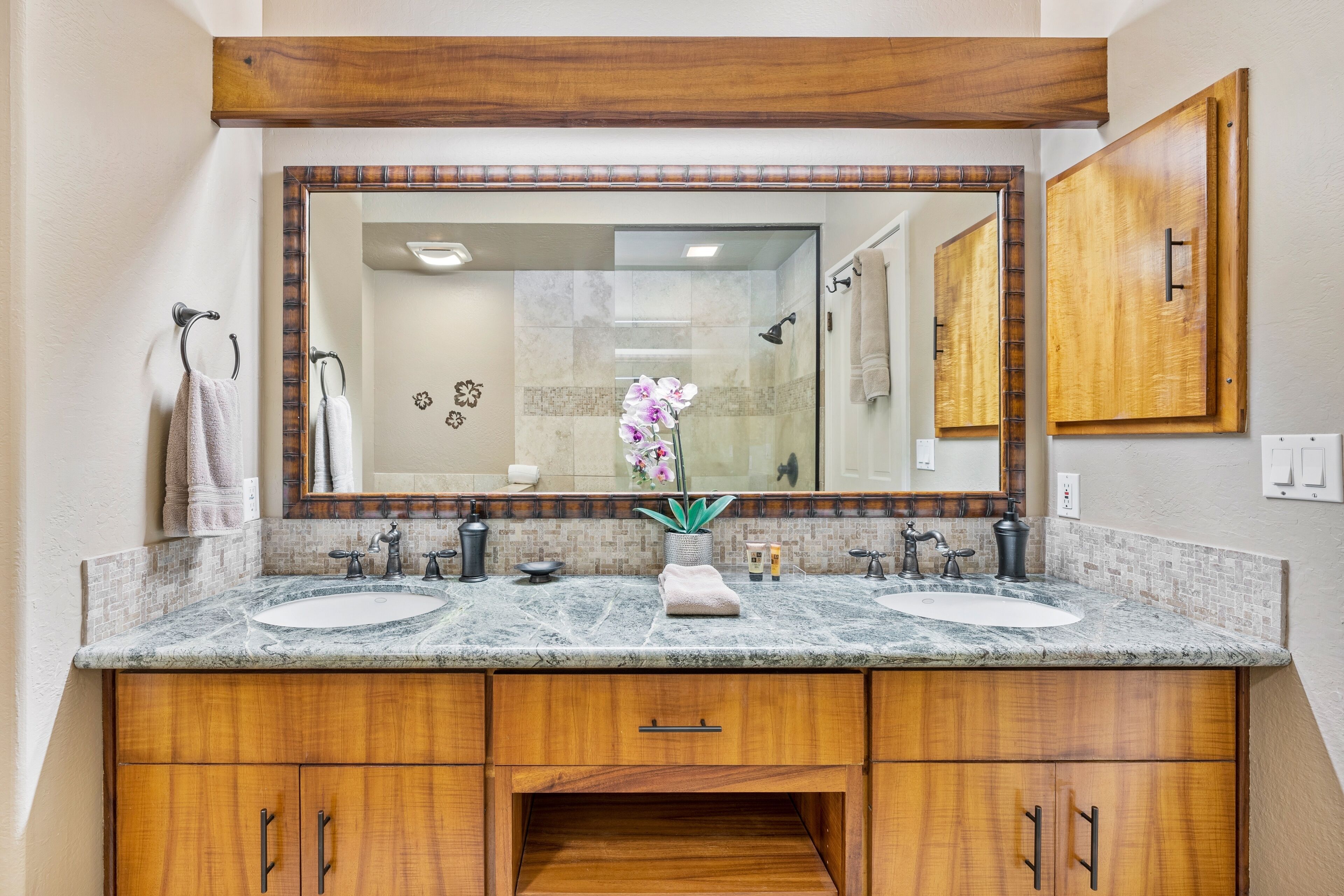 A bathroom with two sinks, a large mirror, wooden cabinets, and a shower area.