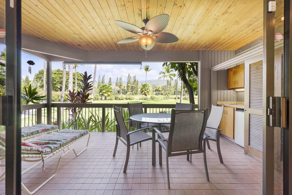 A covered outdoor area with a ceiling fan, a table with chairs, and a view of a golf course.
