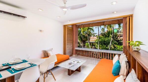 Una habitación moderna con zona de comedor, sofá y balcón con vistas a palmeras.