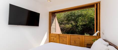 A bedroom with a large window, a flat-screen TV mounted on the wall, and a bed with white bedding.