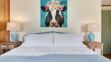 Une chambre à coucher avec un lit, deux tables de chevet avec des lampes et un tableau mural représentant une vache entourée de fleurs.