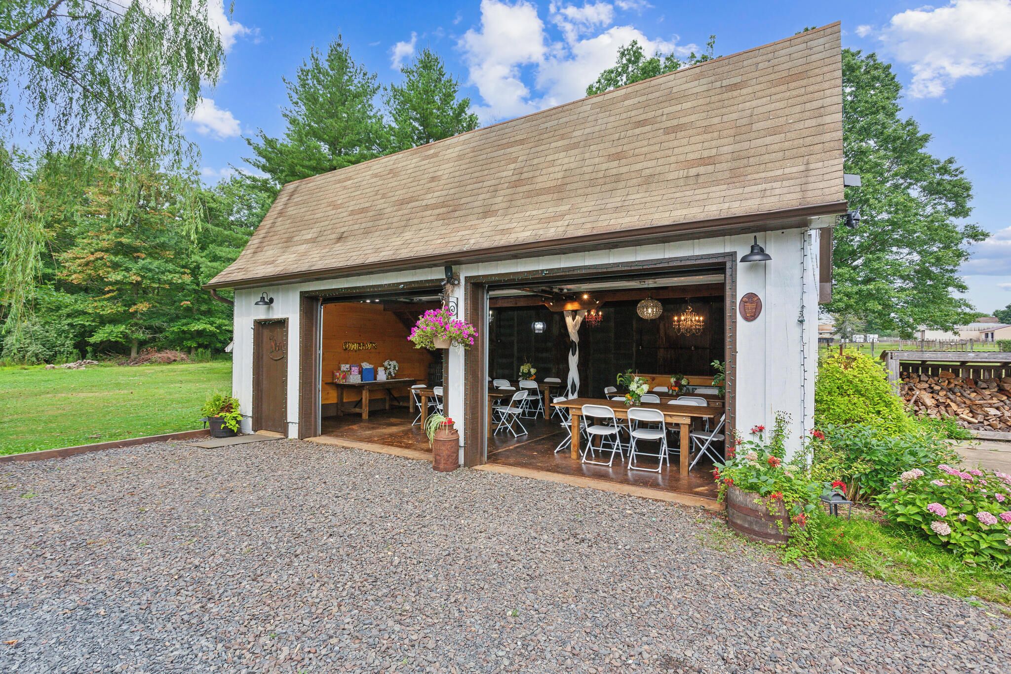 A building with a gravel driveway, a covered outdoor seating area with tables and chairs, and a large open garage door.