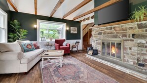 Una sala de estar acogedora con chimenea de piedra, un sillón rojo y un ventanal con vistas a la vegetación.