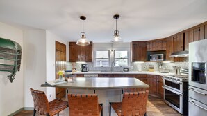Una cocina con gabinetes de madera, una isla central con taburetes de bar, electrodomésticos de acero inoxidable e iluminación colgante.
