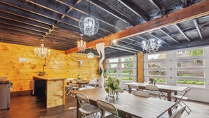 Un comedor rústico con mesas y sillas de madera, candelabros y vistas al exterior a través de amplias ventanas.
