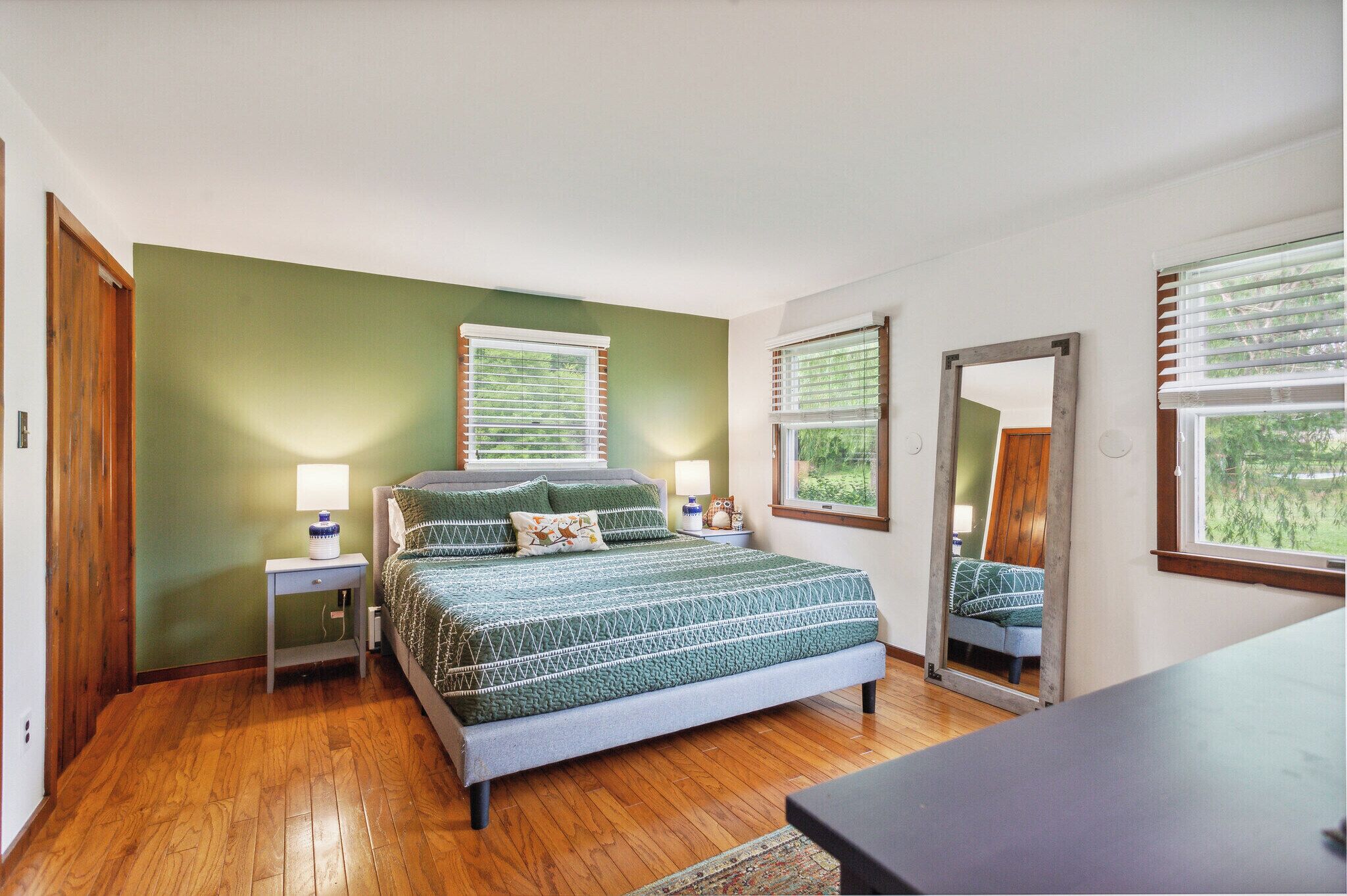A bedroom with a bed, two bedside tables, a mirror, and a window with blinds.