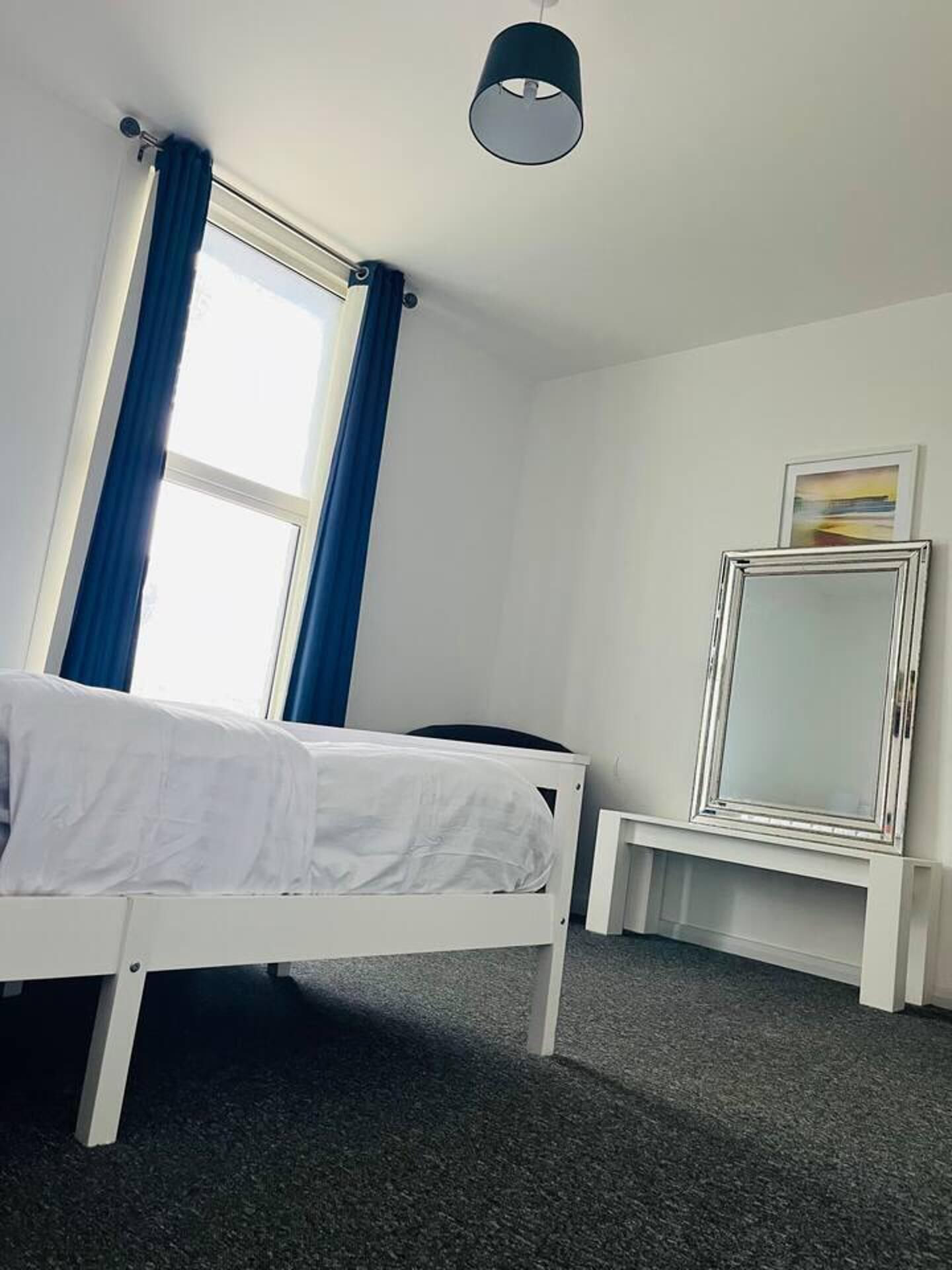 Een slaapkamer met een bed, bureau, stoel, spiegel en een raam met gordijnen.