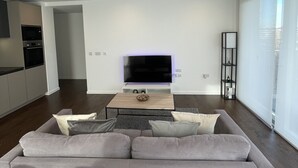 Un salon moderne avec un grand canapé gris, un téléviseur à écran plat et une table basse.