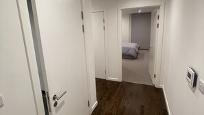 Un couloir avec un plancher en bois, des murs blancs et des portes fermées.