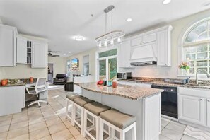 A spacious kitchen with white cabinets, a granite countertop, and a central island with bar stools.