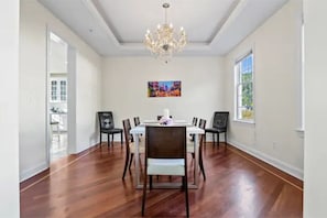 A dining room with a white table and chairs, a chandelier, and a colorful painting on the wall.