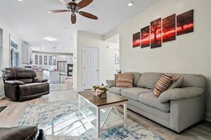 A modern living room with a leather sofa, a glass coffee table, and a ceiling fan.