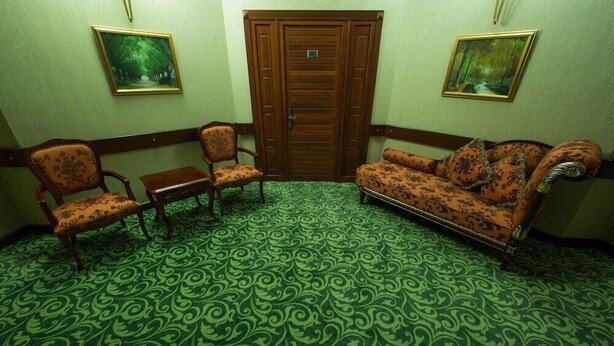 A room with a patterned green carpet, two wooden chairs, a sofa, and two framed pictures on the walls. - Qafqaz Resort (Gabala)