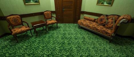 Una habitación con alfombra verde estampada, dos sillas de madera, un sofá y dos cuadros en las paredes.