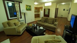 A living room with two sofas, a coffee table, and a television. There is a kitchen in the background with wooden cabinets and a refrigerator. - Qafqaz Resort (Gabala)