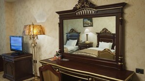 A hotel room with a large mirror, a desk with a lamp, a television, and a bed with a headboard. - Qafqaz Resort (Gabala)