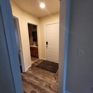 A hallway with a wooden floor, a white door, and a bathroom visible in the background. - One Bedroom Apartment in Kalamazoo with View (Kalamazoo)