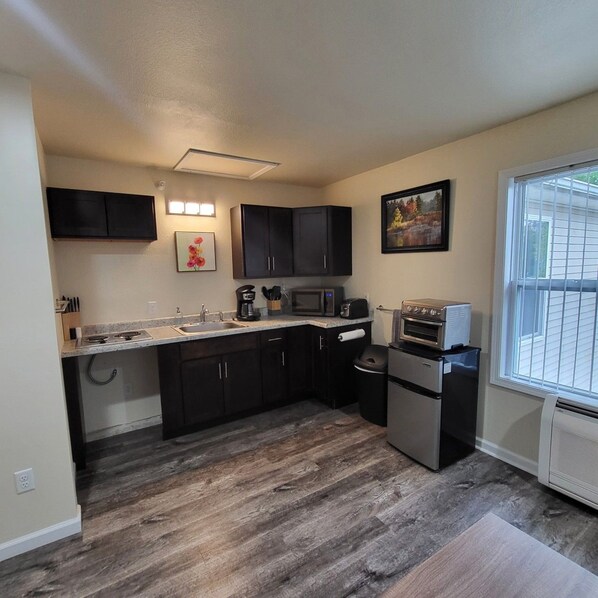 A compact kitchen with dark cabinets, a microwave, a toaster, and a small refrigerator.