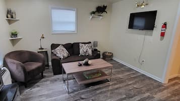 Un salon comprenant un canapé, un fauteuil, une table basse et un téléviseur à écran plat fixé au mur.