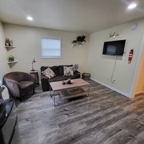 A living room with a sofa, armchair, coffee table, and a flat-screen TV mounted on the wall. - One Bedroom Apartment in Kalamazoo with View (Kalamazoo)