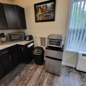 A compact kitchen with dark cabinets, a microwave, toaster, and a small refrigerator. - One Bedroom Apartment in Kalamazoo with View (Kalamazoo)
