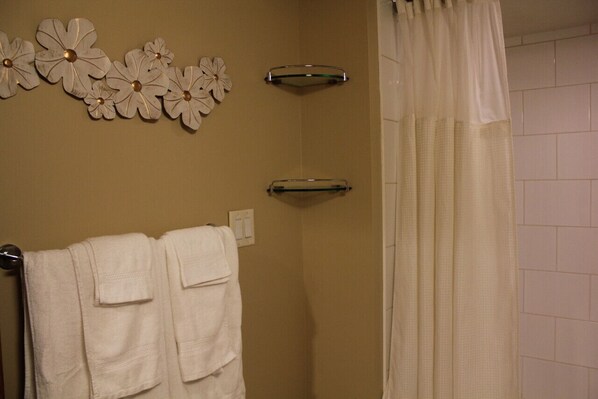 A bathroom with beige walls, a shower curtain, and two towel racks with white towels.