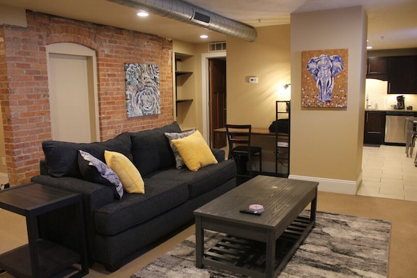 A living room with a dark sofa, a coffee table, and a painting of an elephant.