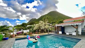 Ein Swimmingpool mit Luftspielzeug, umgeben von einem Garten und einem Haus mit einem Ziegeldach.