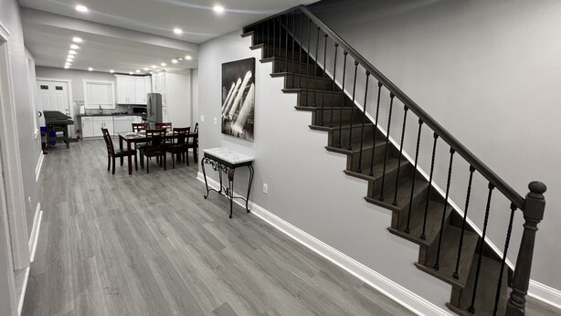 Eine moderne Küche mit weißen Schränken, ein Essbereich mit Tisch und Stühlen sowie eine Treppe mit dunklen Geländern.