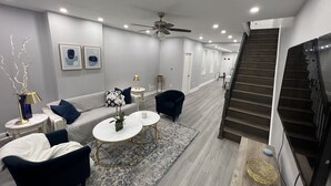 Ein modernes Wohnzimmer mit Sofa, Sesseln, Couchtisch und Treppe.
