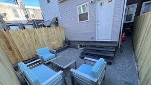 Eine Terrasse mit Tisch und vier Stühlen, ein Holzzaun und eine weiße Tür.