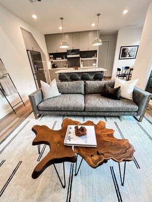 Een moderne woonkamer met een hoekbank, een houten salontafel, en een keuken op de achtergrond.