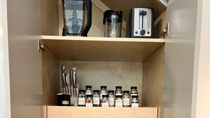 Un armario de cocina con varios estantes que contiene electrodomésticos, utensilios y recipientes de cocina.