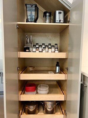 A kitchen cabinet with multiple shelves containing various kitchen appliances, utensils, and containers.