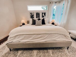 Une chambre à coucher avec un grand lit, deux tables de chevet et une fenêtre avec des rideaux.