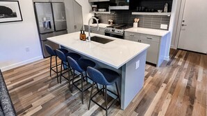 Una cocina moderna con una isla central, taburetes de bar y un refrigerador de acero inoxidable.