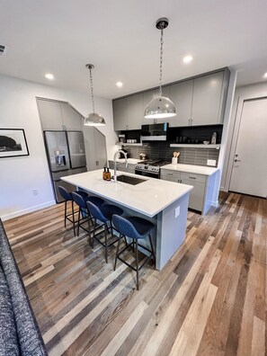 A modern kitchen with a central island, bar stools, and a stainless steel refrigerator.
