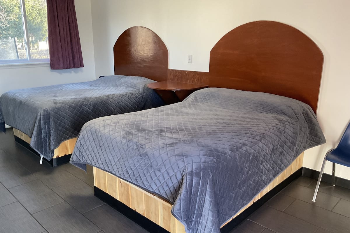 Une chambre avec deux lits, chacun doté d’une tête de lit en bois et d’une literie grise.