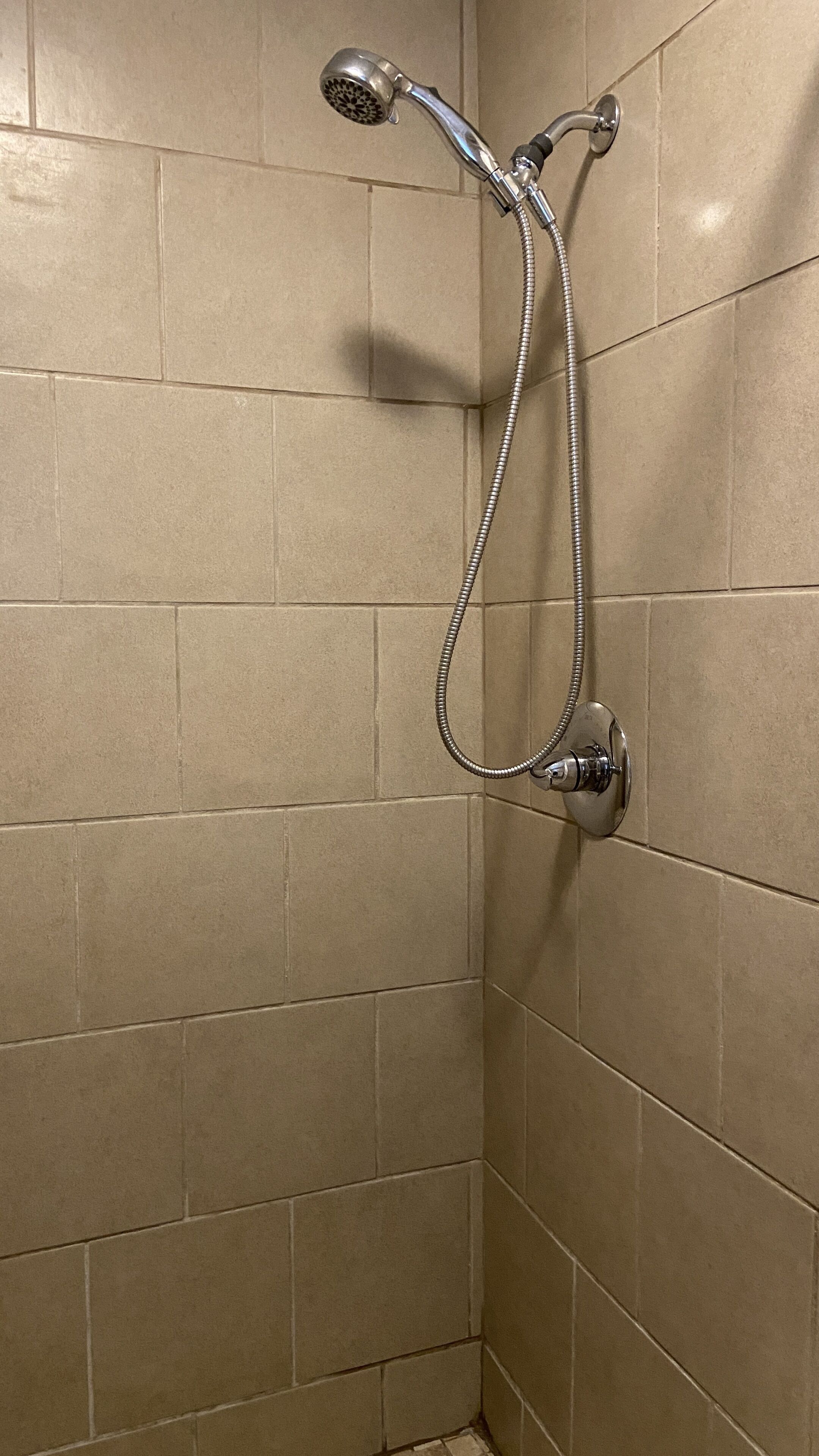 Ducha con cabezal de ducha de mano y llave de control montada en la pared en un baño con azulejos.