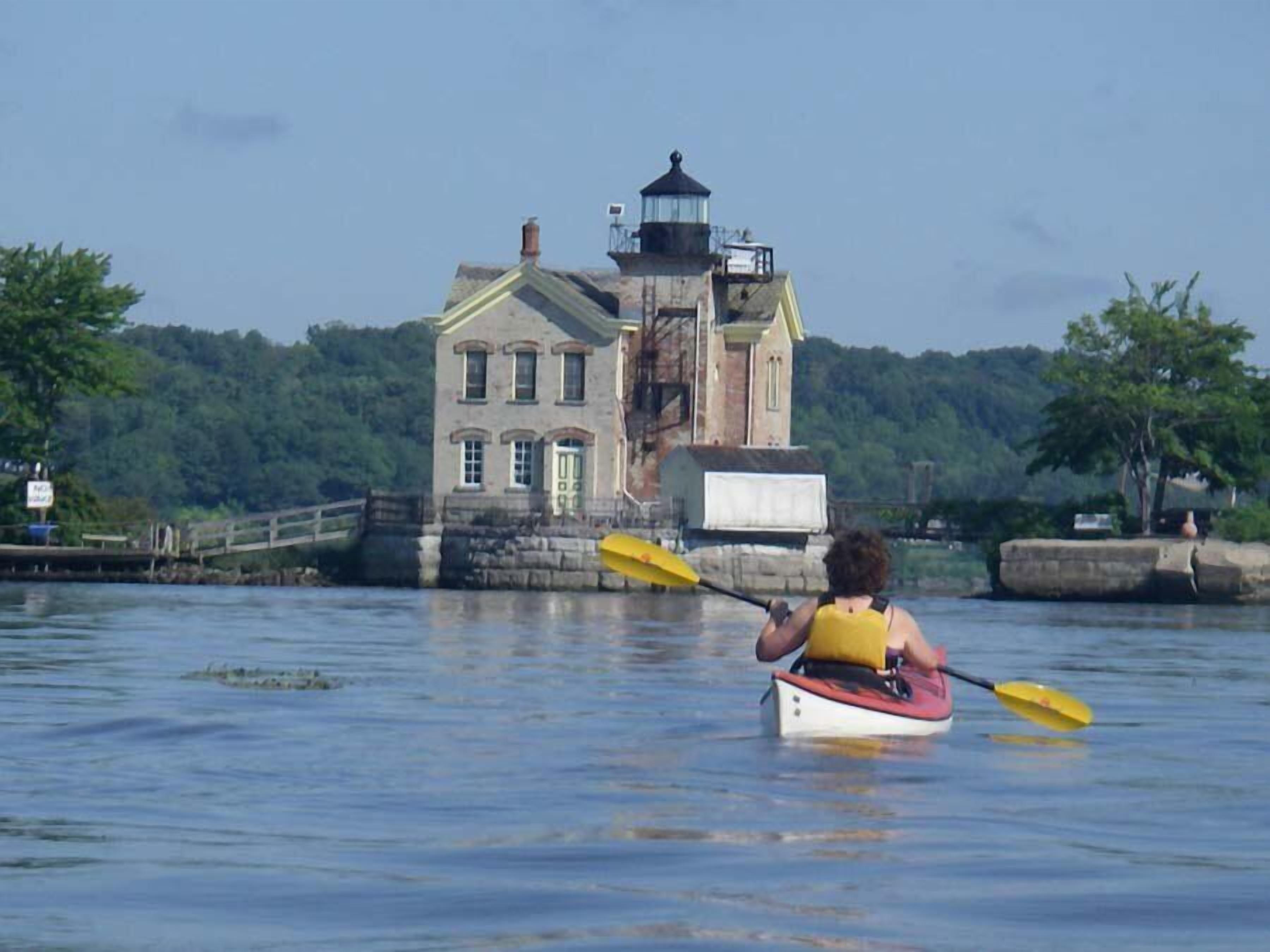 A person kayaking towards a historic building with a lighthouse.