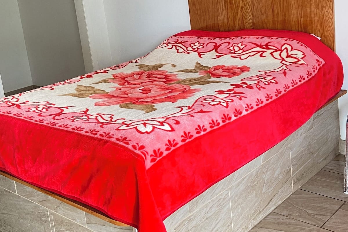 Un lit avec une tête de lit en bois, une couvre-lit à motifs floraux rouge et beige, et un plancher en bois.
