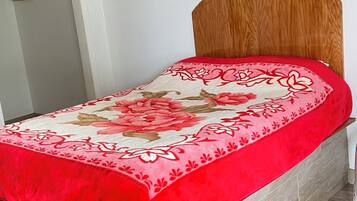 Una cama con cabecera de madera, colcha floral en tonos rojo y beige, y suelo de madera.