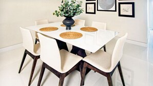 A dining table with six chairs, a vase with green foliage, and framed artwork on the wall.