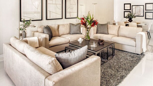 A modern living room with a beige sectional sofa, a coffee table, and a rug. There are framed abstract artworks on the wall.